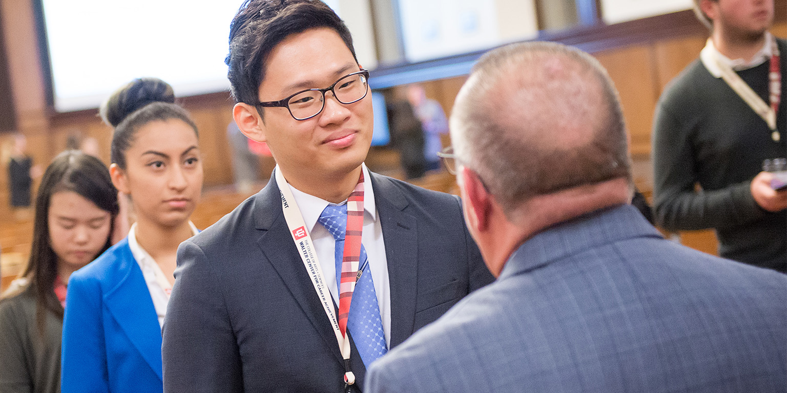 A student smiling as he speaks with an employer at a career fair
